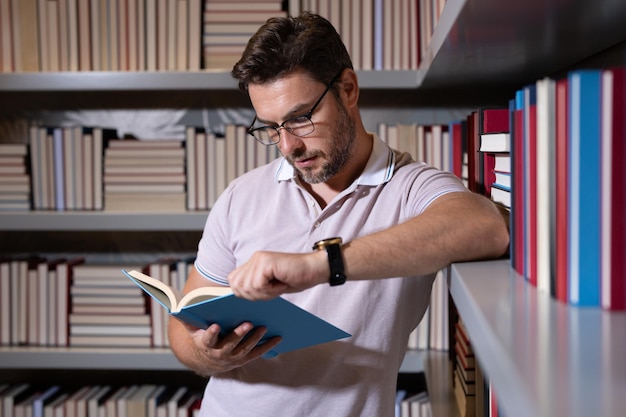 Leraar of professor van middelbare leeftijd in de schoolbibliotheek, leesboek, lerarendagleraar in de klas