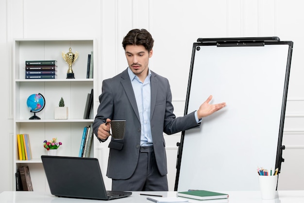 Leraar slimme instructeur in grijs pak in klas met computer en whiteboard met zwarte kop