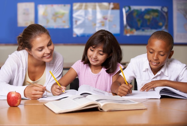 Foto lerarenboeken en schoolkinderen in de klas schrijven of samen leren voor ontwikkeling, studeren of kennis vrouwenkinderen en hulp met notitieboekje met ondersteuning bij lesgeven of onderwijs met glimlach