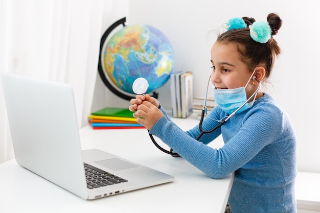 Leren over allerlei dingen op het web. Klein meisje gebruikt het masker als pandemische bescherming. Laptop gebruiken.