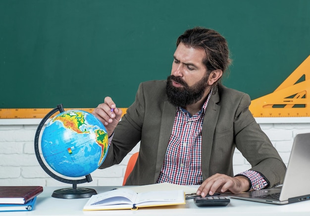 Leren van het onderwerp geconcentreerde man met baard kijken naar aardrijkskunde wereldbol bestuderen van de kaart informeel onderwijs mannelijke student zitten in school klas terwijl les het examen halen niemand kan je stoppen