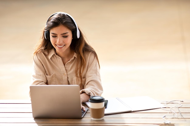 Les online op de campus vrolijke jonge aziatische studente in koptelefoons die op de computer chatten