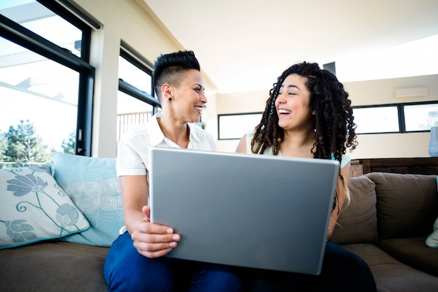 Lesbian couple smiling while using laptop in living room