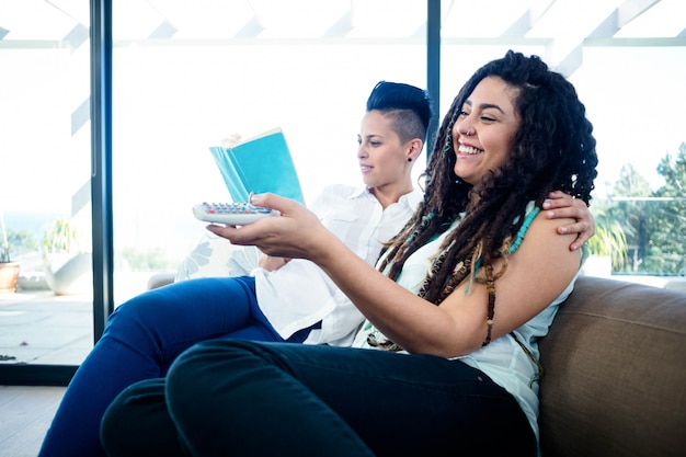 Lesbian couple watching television and reading a book in living room