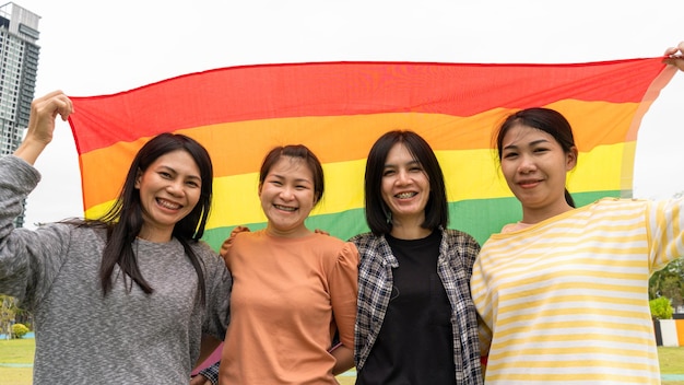 Lesbian and gay 3 people hugging outdoors lgbt hugging by\
rainbow flag happy gay girls gay with lgbtq flag