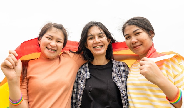 Lesbian and gay 3 people hugging outdoors LGBT hugging by rainbow flag Happy gay girls gay with LGBTQ flag