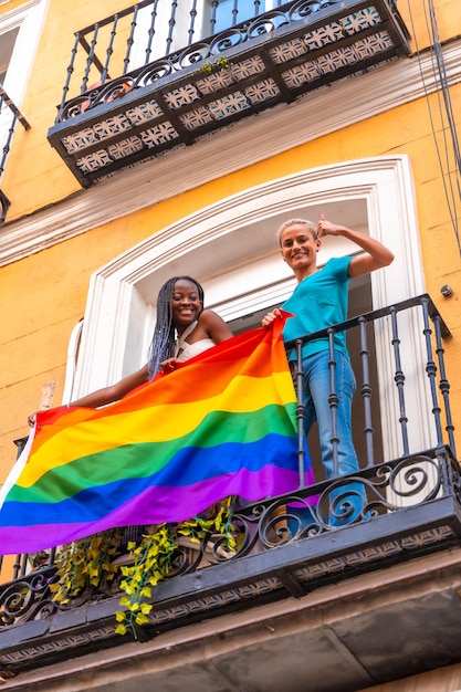 Le coppie di ragazze lesbiche con bandiera lgbt sul balcone a casa festeggiano sventolando l'orgoglio lgbt