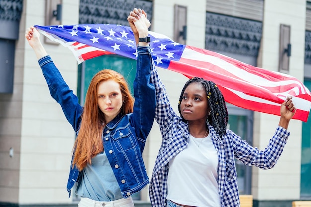 Lesbian redhaired ginger woman and her african american wife holding USA flag in downtown street