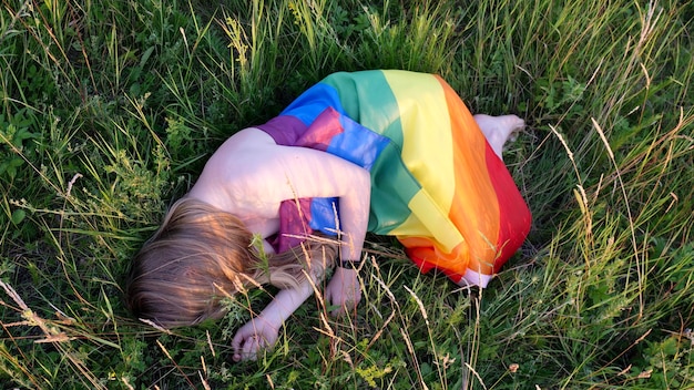 녹색 잔디에 LGBT 깃발에 알몸으로 누워있는 레즈비언 여성 양성애의 날 존엄의 달에 비전통적 오리엔테이션 지지 그 사람이 그리워하고 따돌림으로부터 얼굴을 숨깁니다