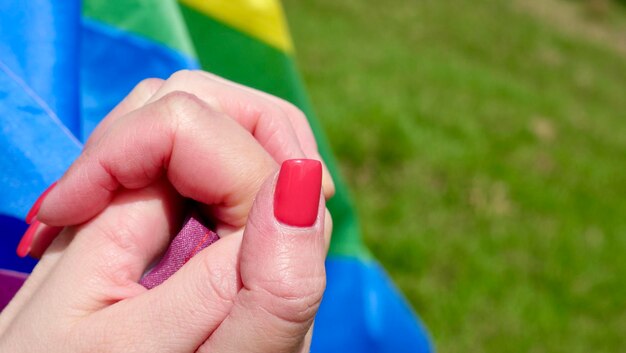 Lesbian women holding hands on LGBT flag background outdoors on a sunny day