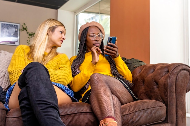 Lesbisch stel van verschillend ras en huidskleur zittend op de bank kijkend naar de mobiele telefoon