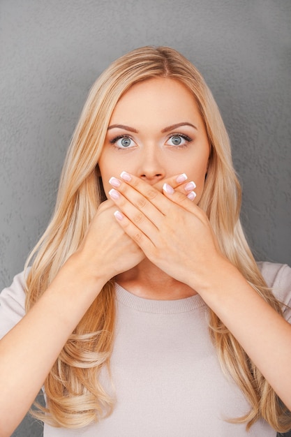 Less information. surprised young blond hair woman covering her mouth and staring at camera