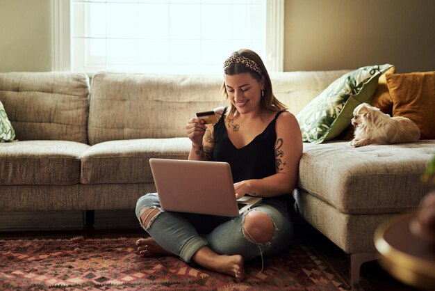 Less queues more relaxing Shot of a young woman using a laptop and credit card in her living room at home