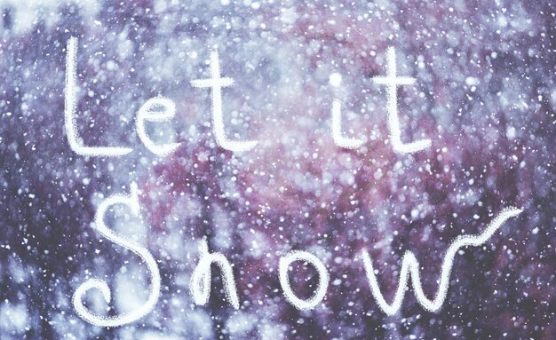 Photo let it snow, written by hand on the snowstorm winter background, toned.