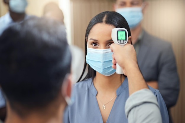 Let me just get your temperature Cropped shot of an attractive young businesswoman wearing a mask and having her temperature taken while standing at the head of a queue in her office