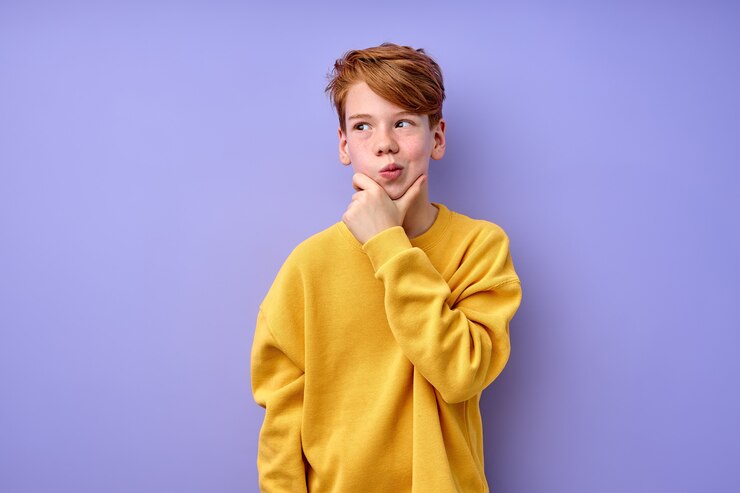 Photo let me think. thoughtful clever redhead schooler in yellow shirt with puzzled serious expression, child thinking doubting, making choice. indoor studio shot isolated on purple background