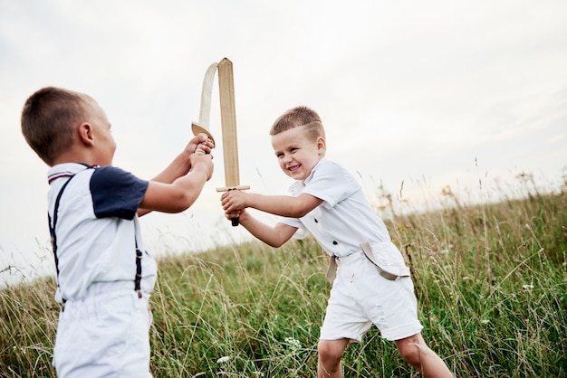 Let's fight like real warriors. Two kids having fun playing with wooden swords in the field.