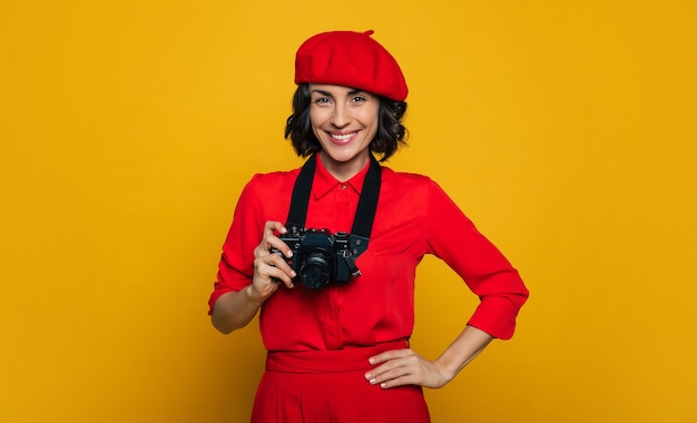 Let's photo some sights! smiley woman on her holiday dressed in a red suit, carrying a camera on a strap on her neck, standing with her left hand on her side.