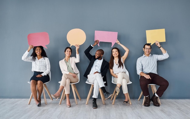 Let us deliver your good news Portrait of a group of businesspeople holding speech bubbles while sitting in line against a grey background