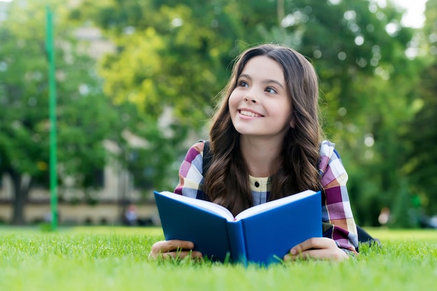 あなたの創造力を調査させてください。幸せな子供は緑の草の上に横たわって本を読んだ。読書教育。本の学習。学校図書館。文学のレッスン。想像力と空想。知識の日。