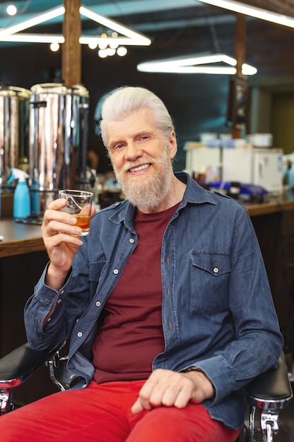 Lets celebrate. Joyful mature man holding glass in right hand while looking straight at camera