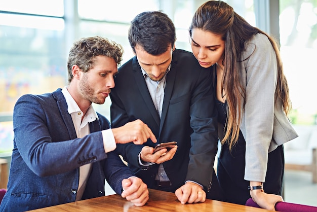 Lets enjoy connectivity together Cropped shot of businesspeople using a cellphone together indoors