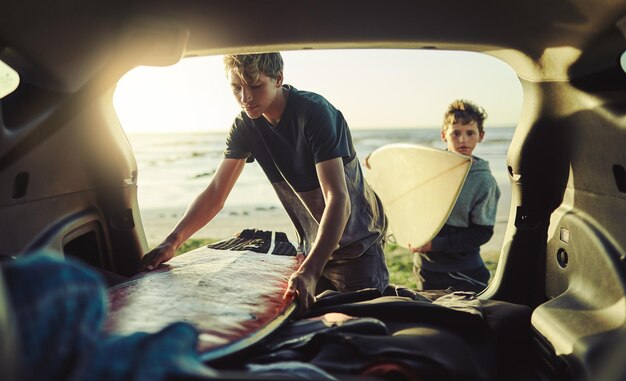 写真 これらのボードにワックスを塗ってもらいましょう2人の若い兄弟がビーチで車の後ろからサーフボードを降ろしているショット