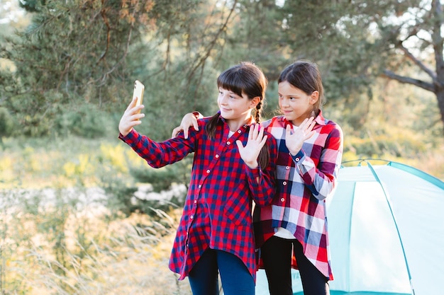 Lets go camping Family camping Reach destination place Cheerful teenage girls talking on a video call looking at the phone screen in the middle of a pine forest near tent Wanderlust discovery