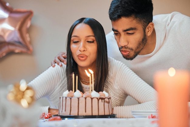 Lets make a wish before we cut the cake. Shot of a young couple blowing candles on a cake while celebrating a birthday at home.