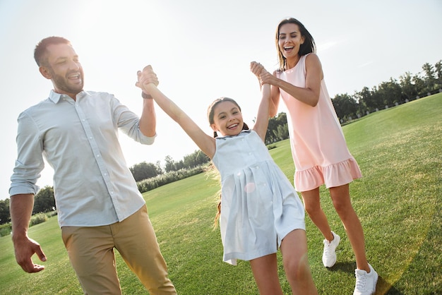 Giochiamo a tutta lunghezza con genitori giovani e felici che trasportano la loro figlia e sorridono mentre