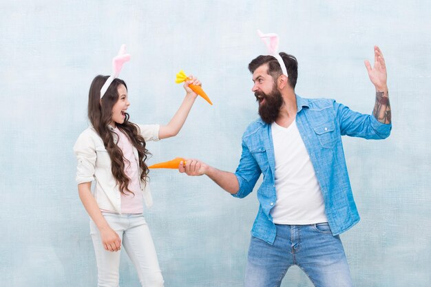 楽しさと幸せを一緒に遊ぼう父と娘はニンジンの春のホリデーパーティーを開催しますウサギの衣装で小さな子供の女の子とお父さん健康食品イースターニンジンの戦い幸せな家族はバニーの耳を着用します
