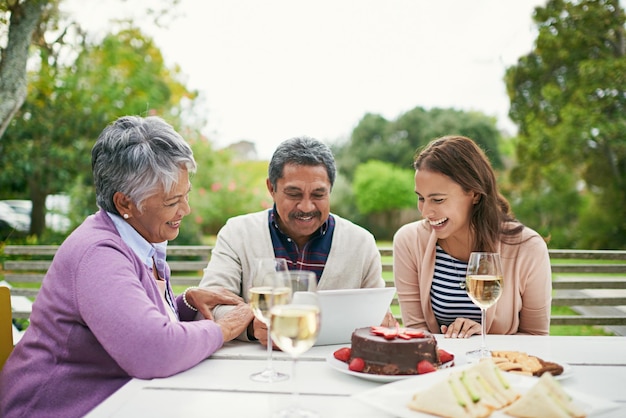 この誕生日の自撮り写真をソーシャルメディアに投稿しましょう。外で昼食をとっているときに家族にタブレットで何かを見せている年配の男性のトリミングされたショット