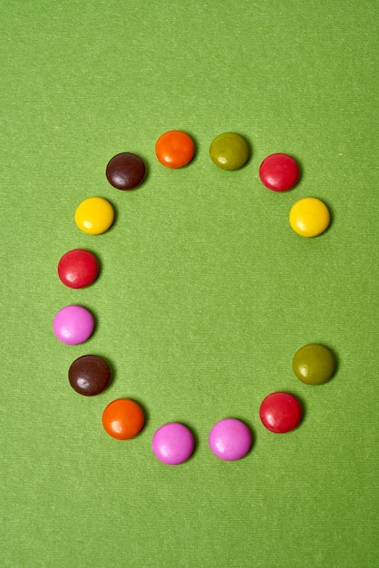 Letter C geschreven met gekleurde ronde chocoladesuikergoed op groene achtergrond.