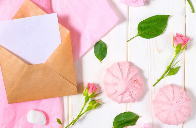 Letter, envelope and a present in eco paper on white background. Wedding invitation s or love letter with pink roses.