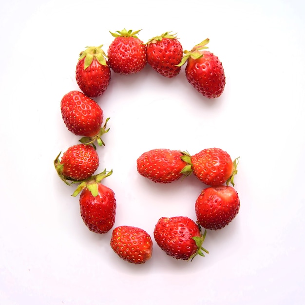 Letter G of the English alphabet of red fresh strawberries on white background