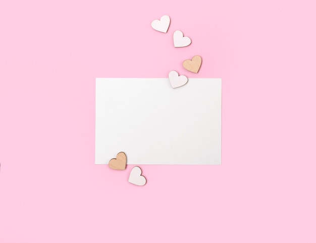 Letter or greeting card with wooden hearts on pastel pink table