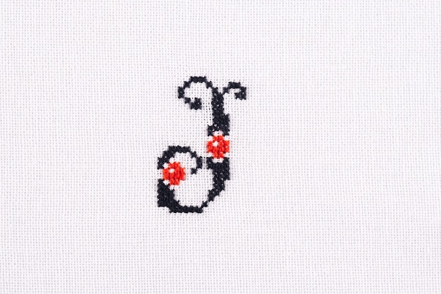 Photo letter j of embroidered cross stitch latin alphabet linen fabric handmade