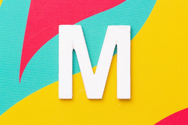 Letter M of the alphabet on colored background top view