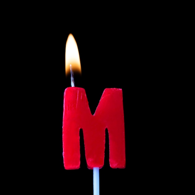 Letter M celebration birthday candle against a black background