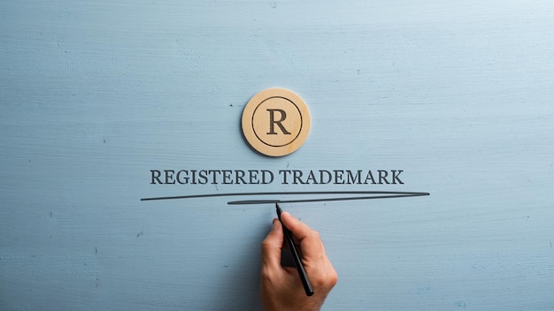 Photo letter r cut into wooden cut circle and male hand writing a registered trademark sign under it