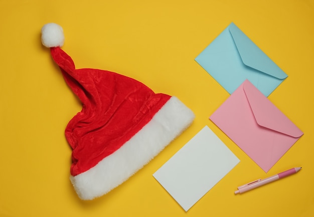 Letter to Santa. Santa hat, envelope with a letter and pen on yellow background. Christmas Flat lay. Top view