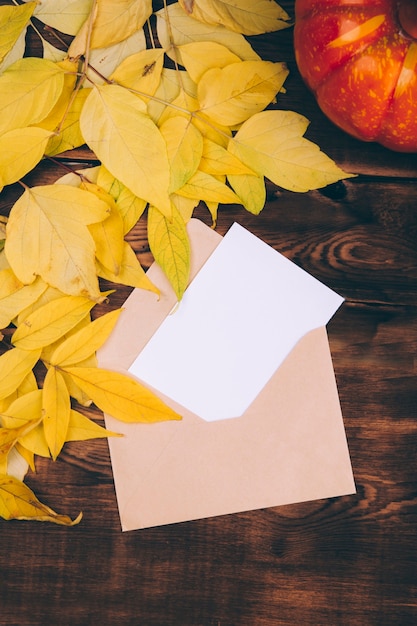 Foto lettera con carta bianca bianca decorata con foglie gialle su fondo in legno