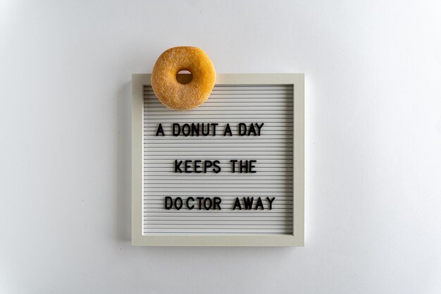 Бумажная доска со словами, которые пишется как пончик в день держит доктора подальше с пончиком на белом