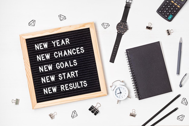 Letterbord met motivatietekst nieuwjaar, kansen, doelen, start, resultaten. Nieuwjaarsviering en resoluties idee. Platliggend met prikbord, planner en kantoorbenodigdheden