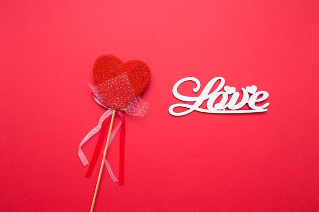 Надпись из деревянных букв любви на красном фоне изолированных. Сердце в виде конфет на палочке.