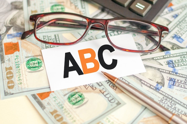The letters A and B and C are written on a white card lying on the bills, glasses, pen and calculator behind