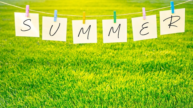 Photo letters summer inscription on pieces of paper hanging with clothespins on rope on grass background