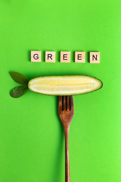 Lettere vegan vegan sano eco cetriolo su una forchetta di legno su una superficie verde