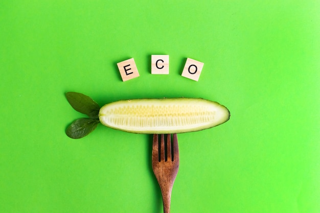 Letters vegan vegan healthier eco cucumber on a wooden fork on a green surface