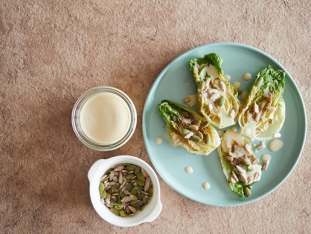 Lettuce hearts in salad with tahini dressing and pumpkin and sunflower seeds. top view on textured brown paper tablecloth